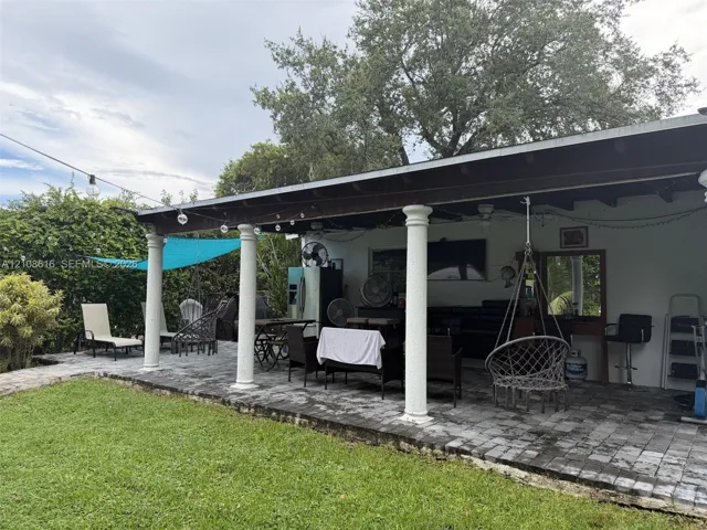 Covered patio featuring stone paver flooring, structural columns, and an expansive lawn