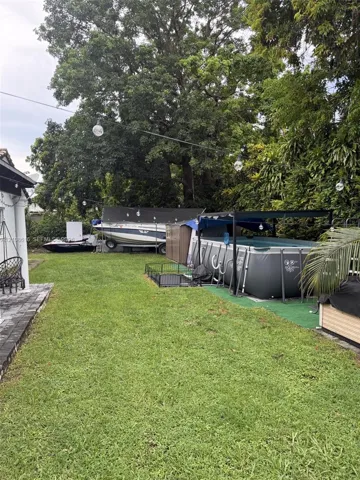 Backyard featuring a grass lawn, mature trees, and overhead string lighting