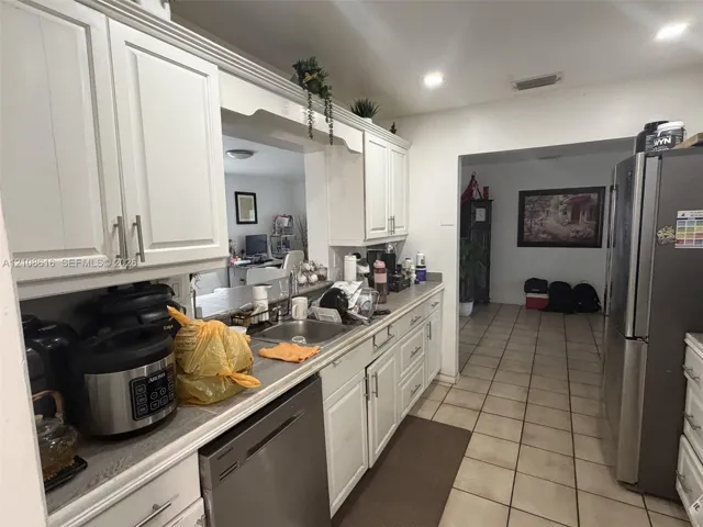 Kitchen featuring white shaker-style cabinetry, stainless steel dishwasher, stainless steel refrigerator, undermount sink, and tile flooring