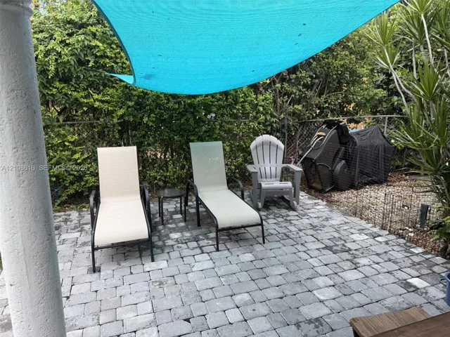 Outdoor patio featuring grey stone pavers, a white cylindrical support column, and a fixed overhead shade canopy
