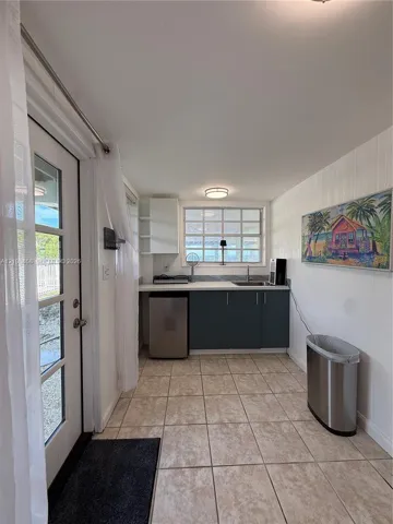Kitchenette featuring dark cabinetry, solid-surface countertops, tile flooring, and a multi-pane window