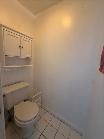 White wall-mounted cabinetry featuring shaker-style doors, an open lower shelf, and ceramic tile flooring
