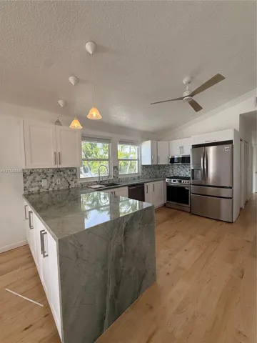 Kitchen featuring a waterfall island, white cabinetry, stainless steel appliances, wood-finish flooring, and a decorative hexagonal tile backsplash
