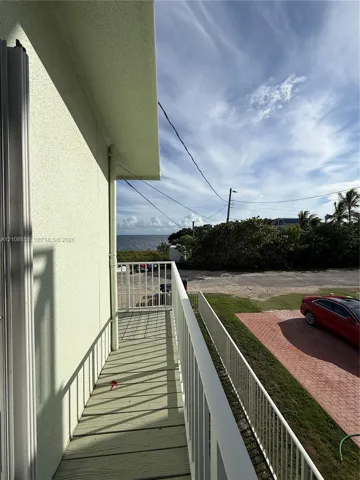 Elevated balcony featuring a painted wood-finish deck and white metal railings with water and horizon scenery