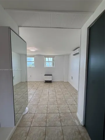 Neutral-toned tile flooring, dual windows, wall-mounted ductless climate control unit, and mirrored built-in closet