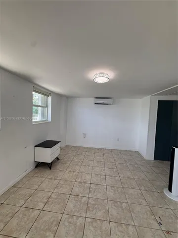 Interior space featuring neutral tile flooring, a wall-mounted mini-split HVAC system, a flush-mount circular light fixture, and a window with a horizontal blind