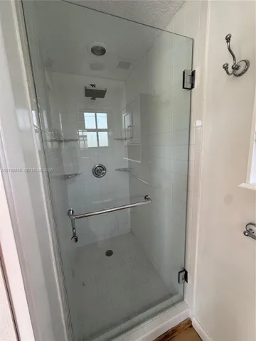 Walk-in shower featuring a frameless glass door, rain-style showerhead, tiled walls, built-in corner shelving, and a chrome towel bar