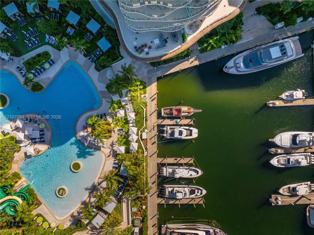 Aerial perspective of a multi-vessel deep-water marina featuring fixed concrete dockage and a large-scale swimming pool with integrated water slide and palm-landscaped deck