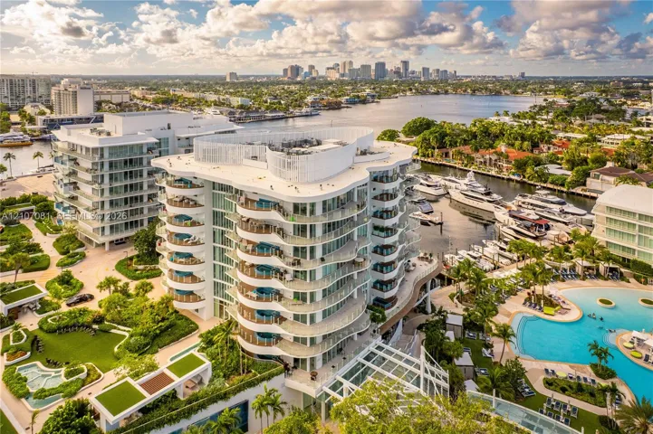 High-rise residential building featuring curved exterior balconies, glass railings, deep-water boat slips, a resort-style swimming pool, and landscaped grounds