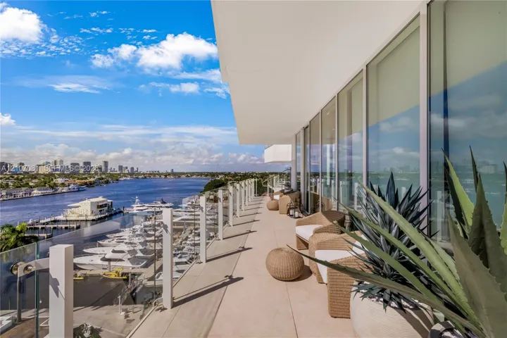 Expansive covered balcony featuring glass railing, smooth concrete flooring, and floor-to-ceiling windows