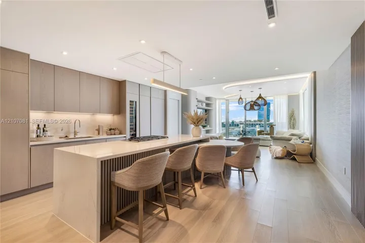 Kitchen featuring floor-to-ceiling cabinetry, a waterfall-edge island, wood-finish flooring, integrated wine refrigeration, and recessed lighting