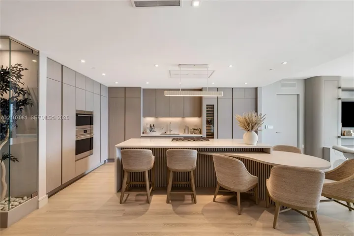 Modern kitchen featuring floor-to-ceiling cabinetry, a central island with integrated seating, built-in stainless steel appliances, wood-finish flooring, and recessed lighting