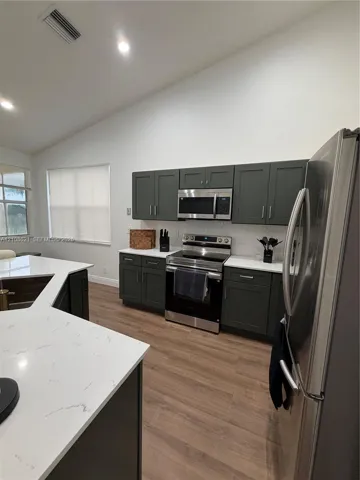 Kitchen featuring dark cabinetry, quartz countertops, stainless steel appliances, a multi-angled island, and wood-finish flooring