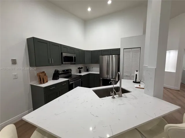 Kitchen featuring dark-toned cabinetry, light-colored countertops with veining, stainless steel appliances, recessed ceiling lighting, and a peninsula with an integrated sink