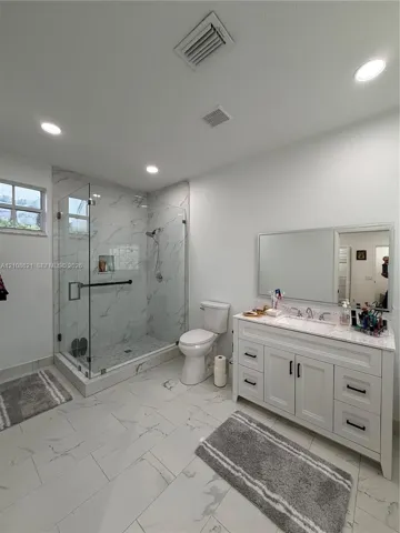 Bathroom featuring a glass-enclosed walk-in shower with tile surround, white vanity with stone countertop, recessed lighting, and large-format tile flooring