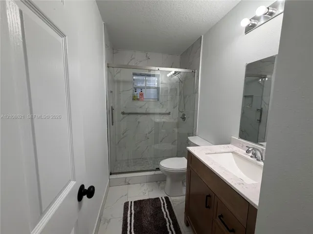 Bathroom featuring a vanity with a light-toned countertop, integrated basin, and matte black hardware, paired with a glass-enclosed shower with stone-patterned wall tile and matching floor tile