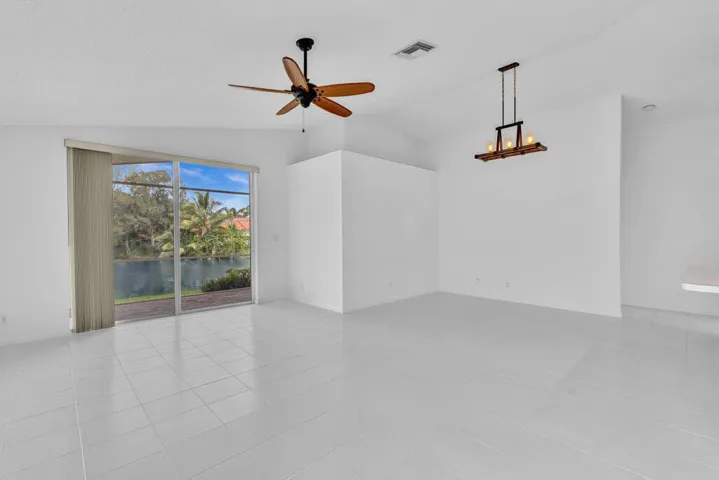 Vaulted ceilings, tile flooring, sliding glass door, multi-blade ceiling fan, and linear pendant lighting fixture