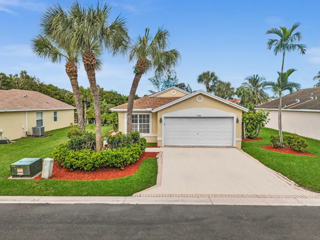 Single-story residence featuring a paved driveway, two-car garage, manicured lawn, and mature palm landscaping
