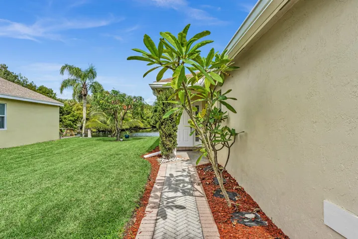 Stucco exterior, herringbone-pattern paver walkway, manicured lawn, established landscaping, and water frontage
