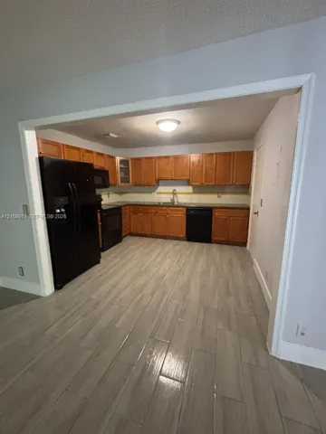 Kitchen featuring wood-finish cabinetry, black appliances, wood-finish flooring, and a stainless steel sink