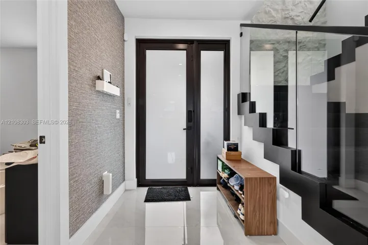 Entryway featuring a black-framed glass entry door, large-format tile flooring, textured wall covering, and a staircase with open risers and a glass railing