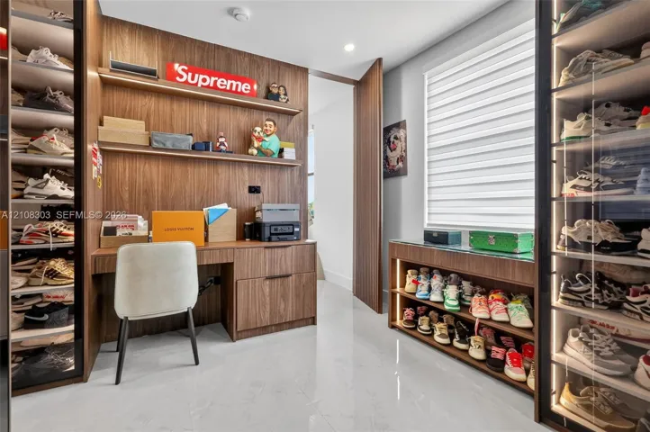 Custom wood-finish cabinetry featuring integrated shelving, built-in desk with drawer storage, glass-front display cases with internal lighting, and light-tone tile flooring