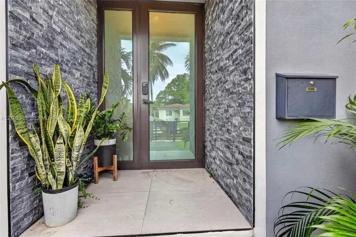 Entryway featuring a full-glass door with dark metal frame, charcoal-toned stacked stone accent walls, large-format tile flooring, and a wall-mounted metal mailbox
