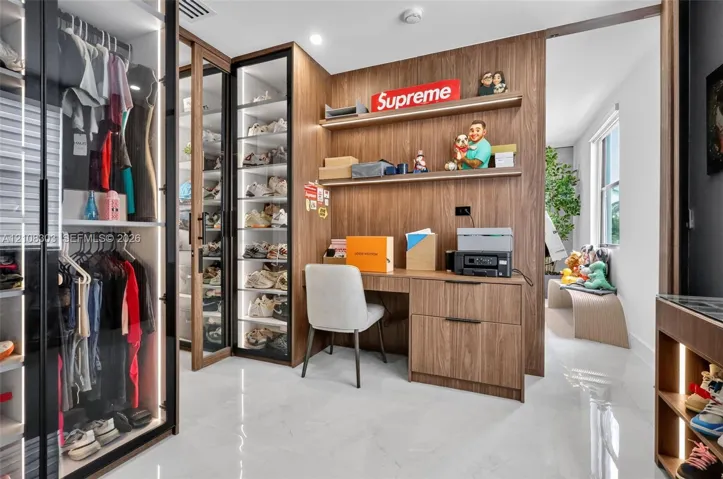 Custom dressing area featuring glass-front cabinetry with integrated lighting, wood-finish wall paneling, and a built-in workstation with floating shelving
