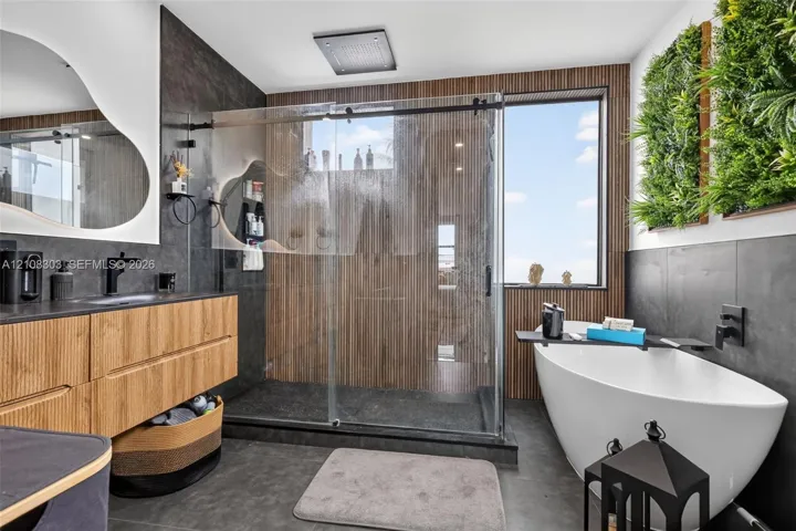 Bathroom featuring a floating wood-finish vanity with a dark countertop, a walk-in glass-enclosed shower with a rainfall showerhead, a freestanding soaking tub, dark large-format wall tile, and vertical wood-slat wall accents