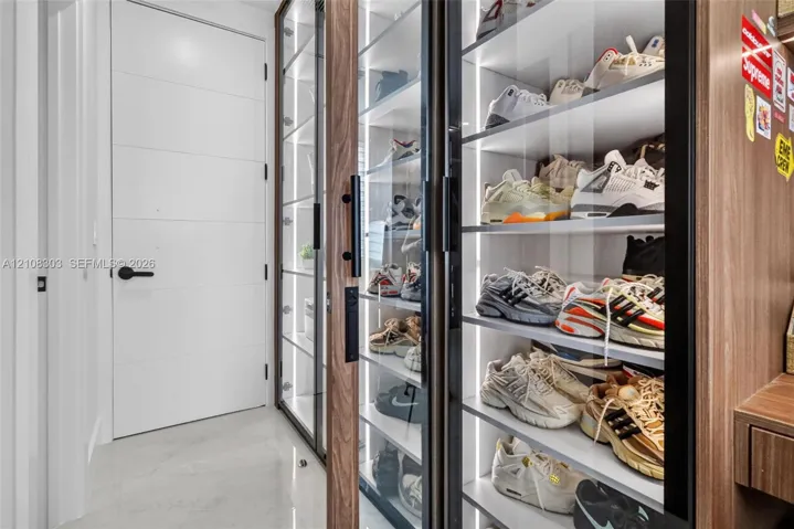 Built-in floor-to-ceiling cabinetry with glass-panel doors, integrated vertical LED strip lighting, wood-finish shelving, and matte black hardware, featuring a solid white interior door with matching matte black handle