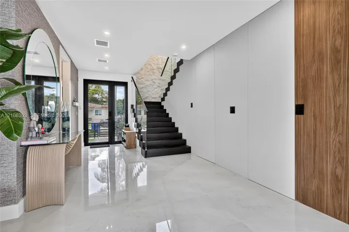 Foyer featuring large-format polished tile flooring, a textured stone accent wall, floating black staircase with glass railing, and integrated wood-finish cabinetry