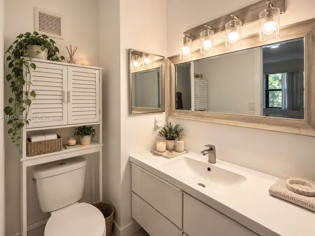 Modern floating vanity with a white countertop, integrated sink, and polished nickel faucet, featuring a large framed mirror with four-bulb light fixture