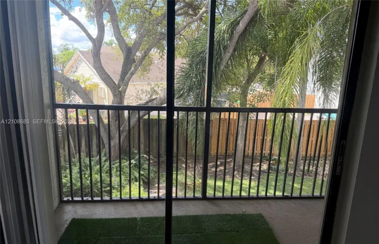 Screened-in balcony featuring black metal railings, concrete flooring, and synthetic turf inlay