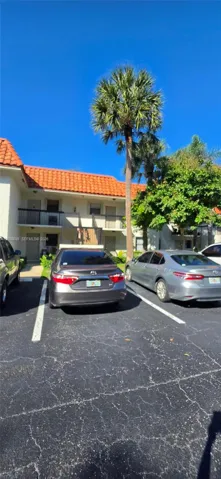 Stucco exterior featuring a terracotta tile roof, second-story balcony with metal railings, and dedicated asphalt parking