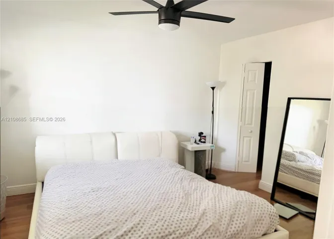 Room featuring wood-finish flooring, a matte black multi-blade ceiling fan with integrated lighting, and a six-panel interior door