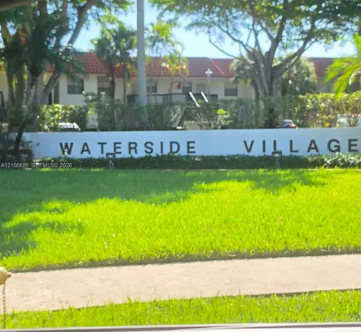 Waterside Village entrance featuring a concrete masonry wall, mature shade trees, and manicured landscaping