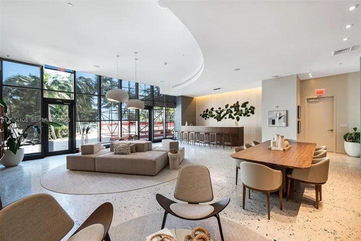 Expansive full-height windows, recessed ceiling lighting, a built-in wood-finish bar, and a dining area with a wood-finish table