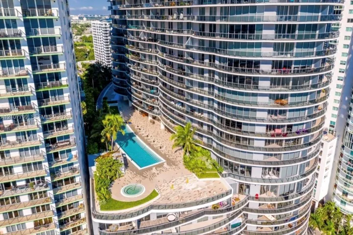 High-rise exterior featuring curved glass balconies, a rectangular swimming pool, a circular spa, tiered hardscaping, and tropical landscaping