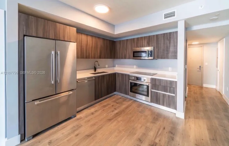 Kitchen featuring wood-finish cabinetry, stainless steel appliances, light-toned stone countertops, and wood-finish flooring
