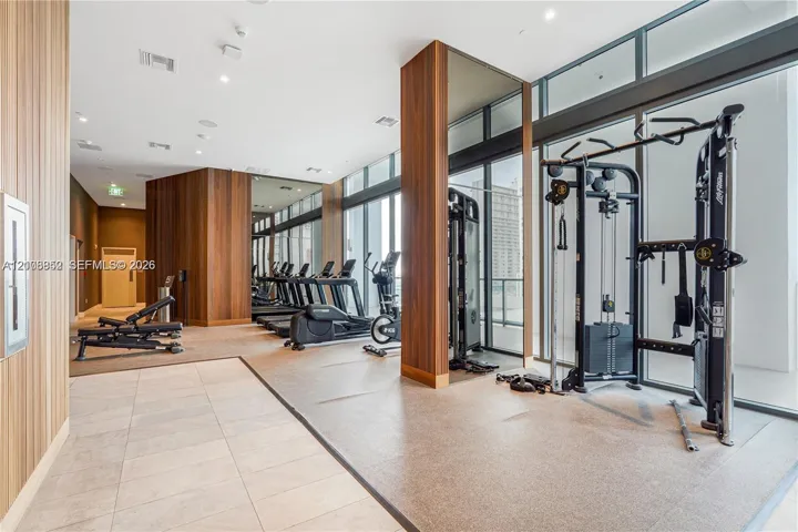 Fitness center featuring floor-to-ceiling glass windows, wood-finish wall paneling, full-height wall mirrors, and recessed lighting