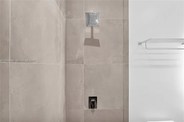 Shower featuring large-format neutral-toned wall tile, a square rainfall showerhead, a built-in single-handle shower valve, and a wall-mounted metal towel rack