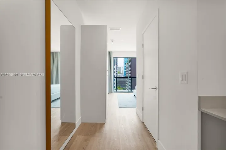 Entryway featuring wood-finish flooring, floor-to-ceiling mirror, neutral wall paint, and flat-panel interior doors