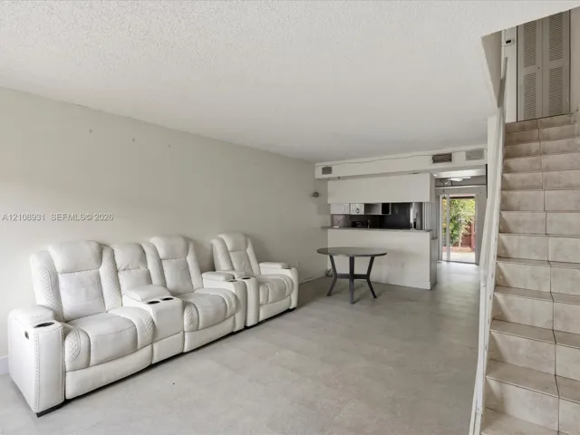 Open-concept interior featuring large-format tile flooring, a kitchen pass-through counter, and a staircase with tiled treads