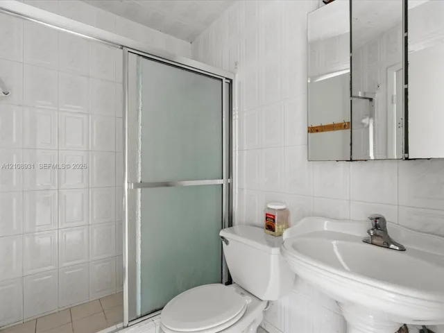 Full-wall ceramic tile surround, pedestal sink with chrome faucet, shower enclosure with sliding glass doors, and mirrored medicine cabinet