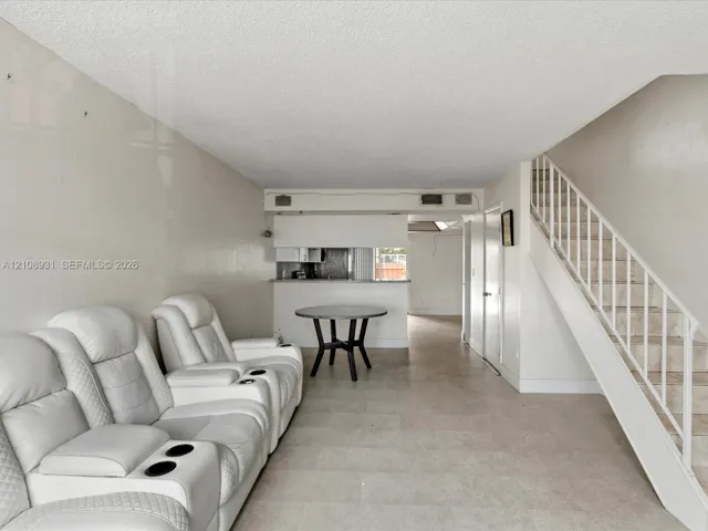Open-concept interior featuring neutral-toned tile flooring, a staircase with a white railing, and a pass-through counter opening to a kitchen area