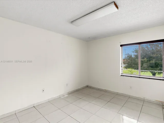 Neutral-toned interior room featuring large-format ceramic tile flooring, a rectangular window with horizontal blinds, and a flush-mount overhead light fixture