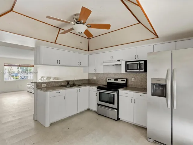 Kitchen featuring a tray ceiling with wood trim, white cabinetry, speckled stone-finish countertops, stainless steel appliances, and a ceiling fan