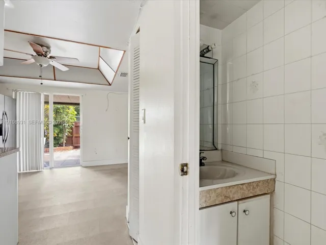Bathroom featuring a single-sink vanity with stone-finish countertop and full-height tiled walls, set within a space showcasing a tray ceiling and sliding glass door access to the exterior