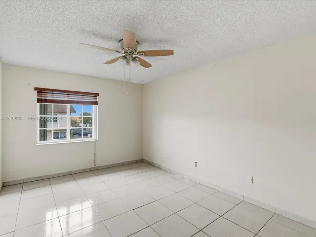 Interior space featuring large-format ceramic tile flooring, a multi-blade ceiling fan with integrated lighting, and a dual-pane window with a horizontal blind