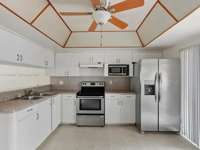Kitchen featuring white cabinetry, speckled stone-finish countertops, stainless steel appliances, and a tray ceiling with wood trim accents